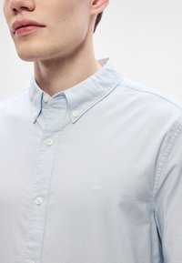 Gaiši zila pogājama krekla ar apkakli, ar baltiem pogām un mazu izšūtu "CK" logotipu kreisajā krūtīs. Gluda tekstūra.