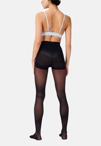 Calze nere opache con vita alta e gambe trasparenti. Il modello indossa un reggiseno azzurro chiaro con spalline sottili. Texture liscia, senza motivi o dettagli.
