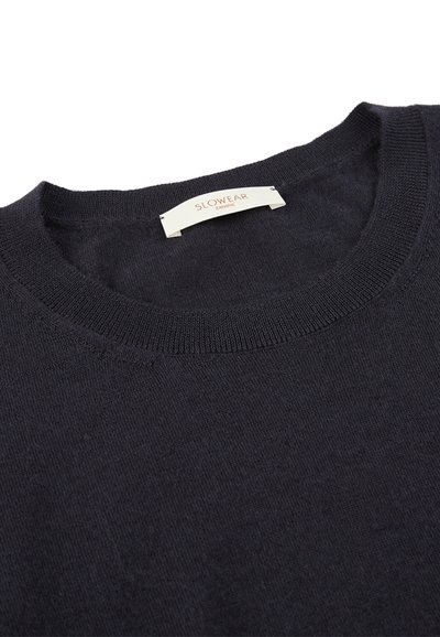 Pull ras du cou bleu nuit en maille douce. Présente un col côtelé et une étiquette avec "Slowear" dans une police subtile.
