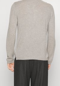 Maglione grigio a maglia con maniche lunghe, colletto rotondo, texture a coste e spacchi laterali all'orlo. Il materiale sembra morbido e leggero.