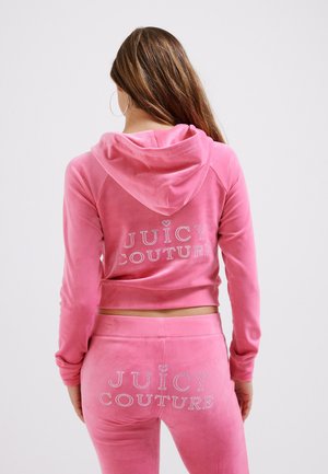 Rozā velūra sporta tērps ar īsā veida kapuci un pieguļošām biksēm. Aizmugurē un priekšpusē dekorēts ar uzrakstu "JUICY COUTURE" no rhinestones. Gluda tekstūra.