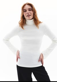 Weißes, geripptes Rollkragenoberteil mit langen Ärmeln, das eine figurbetonte Passform und eine weiche Textur aufweist, kombiniert mit schwarzen Hosen.
