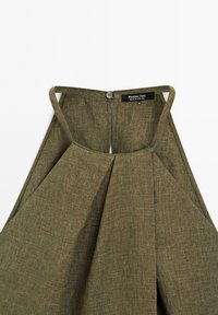 Olivově zelený lněný halter top s designem kapkového výstřihu, plisovaným předním dílem a zapínáním na knoflík v oblasti krku, s viditelným označením značky.
