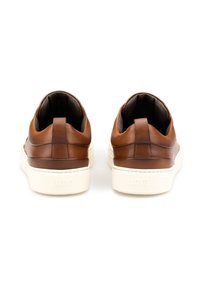 Brązowe skórzane sneakersy o gładkiej powierzchni, białe gumowe podeszwy oraz teksturowane akcenty przy pięcie. Posiadają pętelkę ułatwiającą zakładanie.