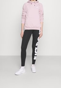 Rosa hoodie med snörning, svarta leggings med vit "JUST DO IT" text, och vita sneakers. Slät tyg, figurnära design.