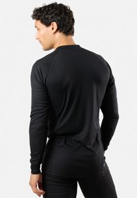 Langärmliges, schwarzes Thermoshirt mit gerippter Textur, kontrastierenden Raglanärmeln und abgerundetem Saum. Der Stoff ist leicht und körpernah geschnitten.