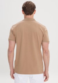 Polo shirt beige à manches courtes, en tissu texturé, avec un col classique. Présente des fentes sur les côtés de l'ourlet pour le confort et la liberté de mouvement.