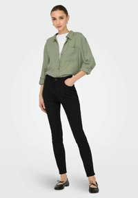 Lichtgroen shirt met lange mouwen, voorvak, gecombineerd met zwarte slim-fit jeans en zwarte flats met strikken. Eenvoudige, casual outfit.