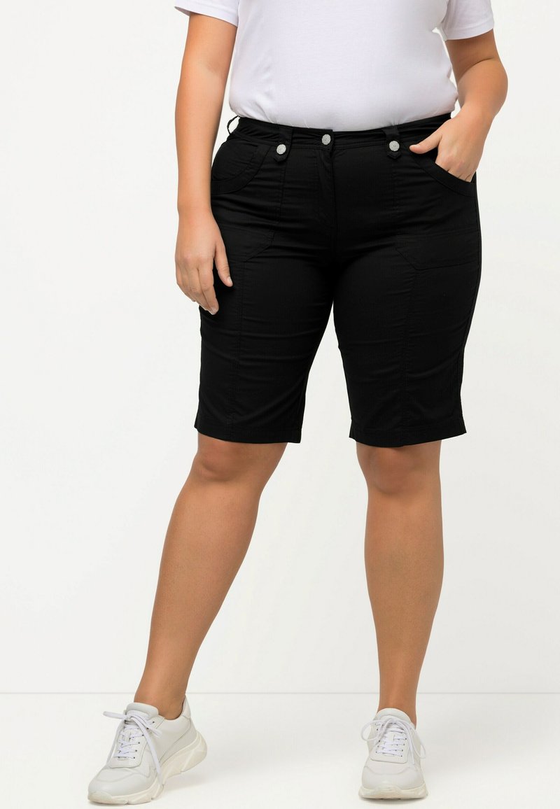 Zwarte shorts met een gestructureerde afwerking, voorzakken en zilverkleurige hardware; gecombineerd met een witte t-shirt en lichte sneakers.