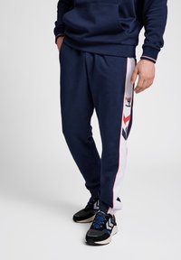 Navyblaue Jogginghosen mit weißen und roten Seitenteilen, elastischem Bund und gerippten Bündchen. Mit einem Logo am linken Oberschenkel und einer lässigen Passform.