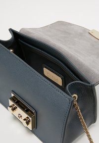 Liten marinblå läderhandväska med texturerad yta, guldfärgad metall och magnetlås. Insidan har ett grått mockafoder.