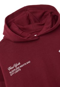Felpa bordeaux con grande collo a barchetta, decorata con testo bianco che recita "New York SLEEPLESS NIGHTS AND CITY LIGHTS" sul davanti. Materiale in cotone.