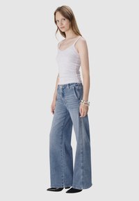 Jasnoszary podkoszulek na ramiączkach zestawiony z wysokimi, szerokimi niebieskimi dżinsami. Materiał wydaje się miękki; dżinsy mają wyblakłe wykończenie i kontrastowe szwy.