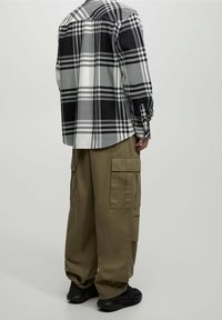 Camicia a quadri bianca e nera con orlo arrotondato, abbinata a pantaloni cargo color oliva con numerose tasche e vestibilità rilassata. Sneakers nere.