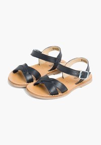 Mustat nahka-sandaalit, joissa on ristiin menevät hihnat, säädettävä nilkkapanta, ruskea sisäpohja ja vaalea ruskea pohja.