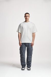 Tricou alb din bumbac supradimensionat, cu mâneci scurte, purtat cu pantaloni cargo gri, care au mai multe buzunare, și adidași alb-negru.
