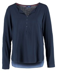 Blusa navy a maniche lunghe con scollatura a V, cinque bottoni decorativi sul davanti e un'orlo inferiore di un blu chiaro a contrasto. Texture morbida.