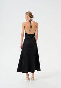 Črna obleka z halter ovratnikom in odprtim hrbtom, z razslojenim krilom in ukrivljenimi šivi. Gladek material z minimalističnim dizajnom, v kombinaciji z svetlimi petami.