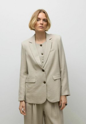 Beige linned blazer med to frontlommer, enkelt knaplukning og slagkraver. Båret over en matchende bluse, der fremviser et tekstureret stof.