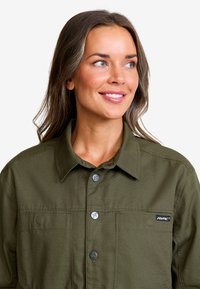 Olivgrön skjorta med knappar i texturerat material, med krage, två bröstfickor och en logolapp på sidan.