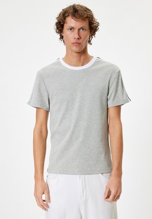 Grå kortærmet t-shirt med struktureret overflade, hvidt rundtalje og sorte detaljer på skuldrene. Blødt materiale, tætsiddende design.