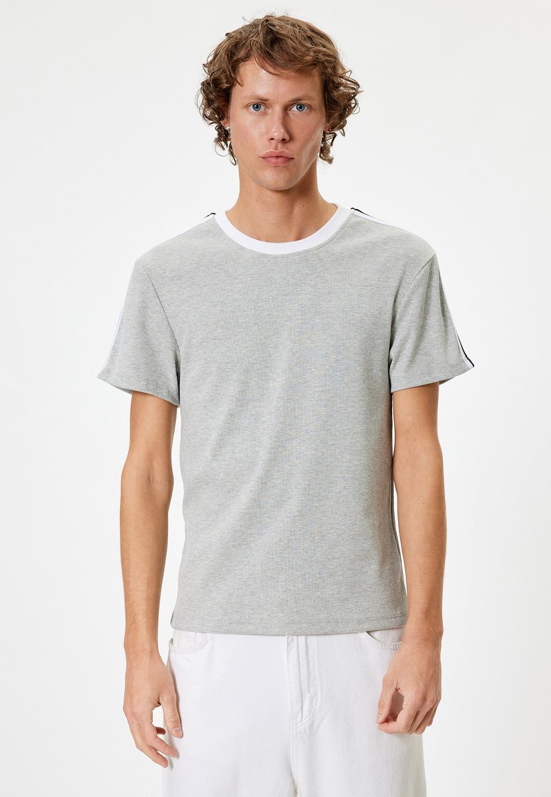 Grå kortærmet t-shirt med struktureret overflade, hvidt rundtalje og sorte detaljer på skuldrene. Blødt materiale, tætsiddende design.