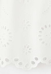Tissu blanc avec des motifs floraux œillets brodés et des bords festonnés, mettant en valeur des détails découpés délicats.
