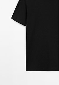 Schwarzes Kurzarm-T-Shirt aus Baumwolle mit Rundhalsausschnitt, flach auf weißem Hintergrund liegend, zeigt linke Seite und Ärmelabschlussnähte.