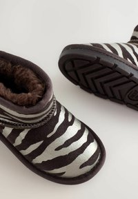 Stivali a strisce zebra neri e argento con un morbido interno peloso. Presentano una suola testurizzata e una forma arrotondata per comfort e calore.