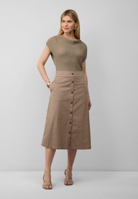 Beige gestricktes Oberteil mit weitem Ausschnitt, kombiniert mit einem Midirock mit Knopfleiste und Taschen. Helle Sandalen in Tan runden den Look ab.