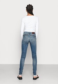 Blå smala jeans med tvättad look, bakfickor med dekorativ söm och en brun läderetikett på midjebandet.