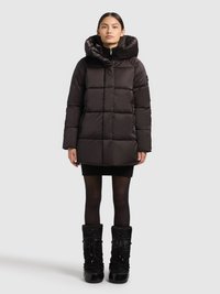 Svart puffjacka med quiltat mönster och hög krage. Har en stor huva, dragkedja framtill och sidfickor. Bärs med en svart kjol och stövlar.