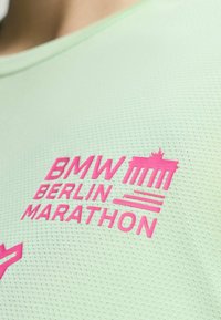 Vihreä kosteutta siirtävä kangaspaita, jossa vaaleanpunaista tekstiä: "BMW BERLIN MARATHON" ja kuva Berliinin portista. Rakennepinnalla.