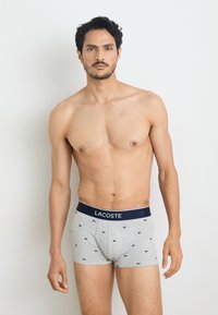 Boxer shorts gris avec une ceinture marine arborant le logo "LACOSTE" et un petit motif marine, fabriqués en coton doux et extensible.