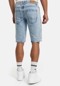 Pantaloni scurți din denim albastru deschis cu spălare estompată, cinci buzunare și croială dreaptă. Completați cu adidași albi și șosete cu dungi.