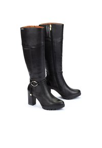 Botas negras hasta la rodilla hechas de cuero liso, con cremallera lateral, tacón grueso y un anillo decorativo cerca del tobillo. Suela de goma para mayor agarre.