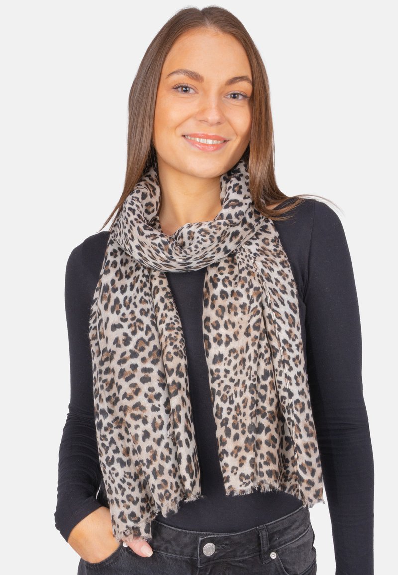 Écharpe en imprimé léopard en tissu doux, avec des taches beiges et noires, bords à franges et design léger, portée autour du cou.