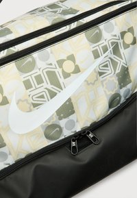 Τσάντα Nike με υφασμάτινο μοτίβο σε πράσινους και κίτρινους τόνους, με έντονο λευκό λογότυπο και μαύρη βάση με διπλά φερμουάρ.