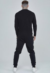 Black long-sleeve shirt and matching joggers, made from soft fabric. Features fitted cuffs, elastic waistband, and may have subtle detailing.