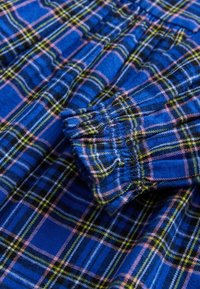 Tissu à carreaux bleu avec des lignes croisées roses, noires, blanches et jaunes, montrant un détail froncé comme un poignet ou une ceinture.