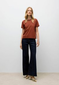 Rød kortærmet t-shirt kombineret med vide mørkeblå jeans og spidse slangeskindsheels. Simpelt design, glat tekstur.