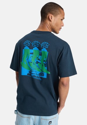 T-shirt en coton bleu marine avec un motif graphique représentant des figures vertes et des fleurs sur un fond bleu. Manches courtes, coupe décontractée.