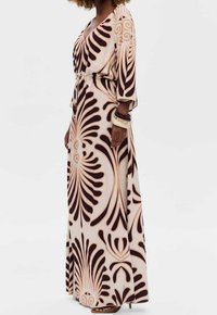 Vestido maxi crema con estampado abstracto marrón. Tela ligera y fluida con escote en V profundo y mangas tres cuartos. Detalle de cintura anudada.