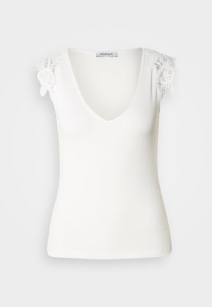 Valge ribaga särk V-kaelusega ja lillelise pitsiga kaenlaaugudel. Sile tekstuur, kehakujuline disain. Brändi silt nähtav seest.