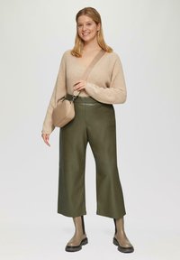 Beige gebreide trui met lange mouwen, olijfgroene leren culottes en enkellange bruine laarzen. Kleine bruine schoudertas.
