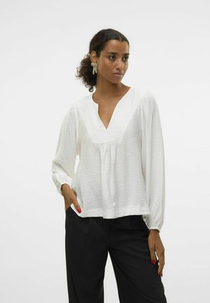 Chemisier blanc à manches longues avec un col en V et un tissu texturé. Présente des détails froncés à l'avant et une coupe décontractée et ample. Assorti à un pantalon noir.