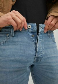Vaqueros de denim azul claro con cierre de cremallera y botón, que cuentan con un diseño clásico de cinco bolsillos y un ligero desgastado en la tela.