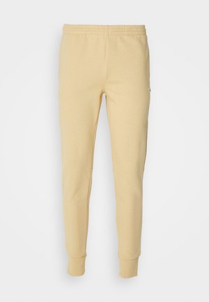 Beige taps toelopende joggingbroek met elastische tailleband en boorden, gemaakt van zachte stof, getoond op een effen achtergrond.