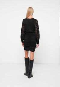 Μαύρο φόρεμα από δαντέλα με μακριά μανίκια, σχεδίαση με πτυχώσεις και εφαρμοστό σιλουέτα. Συνδυασμένο με μαύρες μπότες με τακούνι μέχρι το γόνατο.