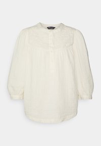 Blouse blanche à manches longues en tissu léger, avec un col rond, une fermeture à boutons sur le devant, et des détails brodés sur le corsage.
